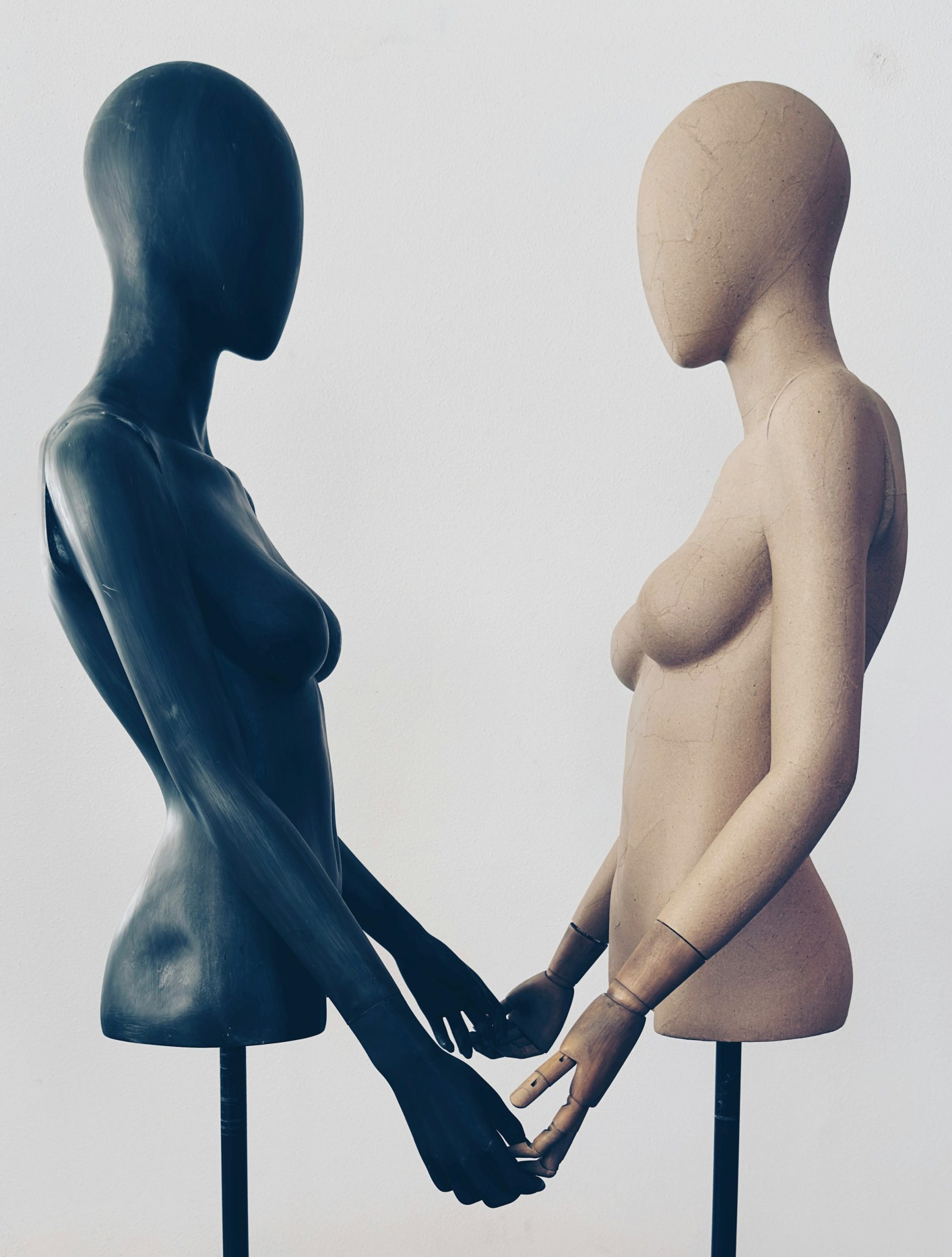 A black mannequin and a white mannequin standing side by side and holding hands, representing peaceful coexistence.